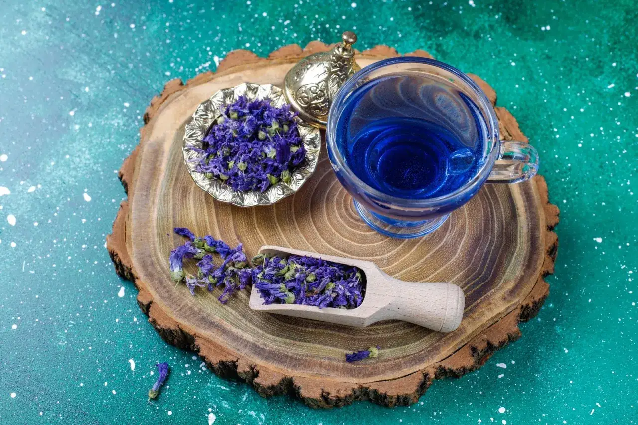 Té azul vibrante preparado con aciano, mostrando sus propiedades relajantes. Flores secas en cuenco y pala de madera.
