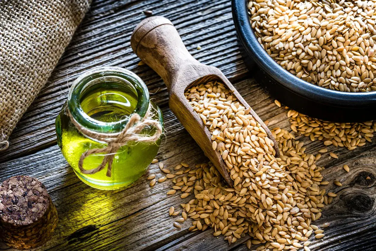 Aceite de lino en un frasco de vidrio, junto a semillas de lino en una cuchara de madera. Descubre las increíbles propiedades del aceite de lino.