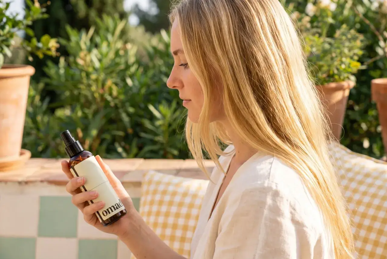 Mujer rubia con un spray para aclarar el pelo de forma natural, disfrutando del sol en un jard&iacute;n.