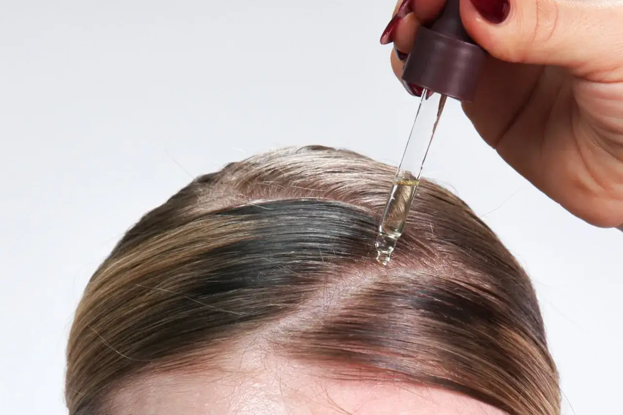 Una mano aplica aceite de ricino para el pelo en la ra&iacute;z.
