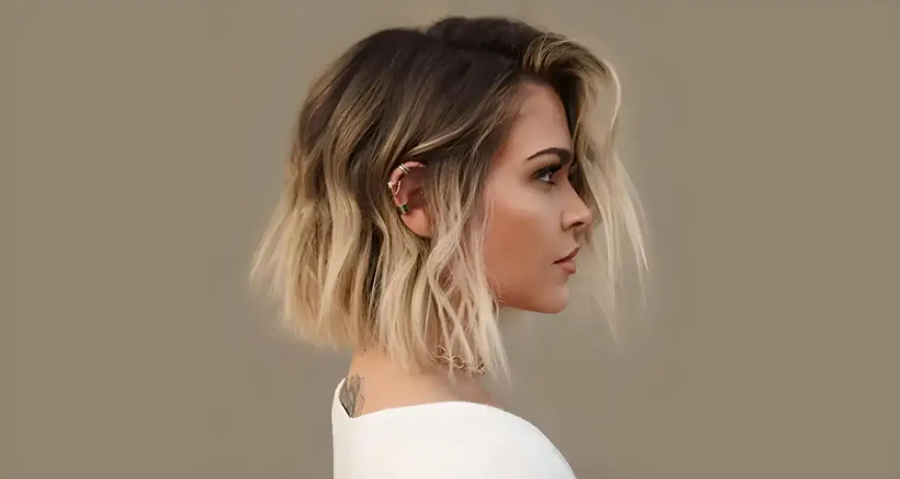 Perfil de mujer con cabello corto y ondulado con mechas californianas, luciendo aretes y un collar delicado.
