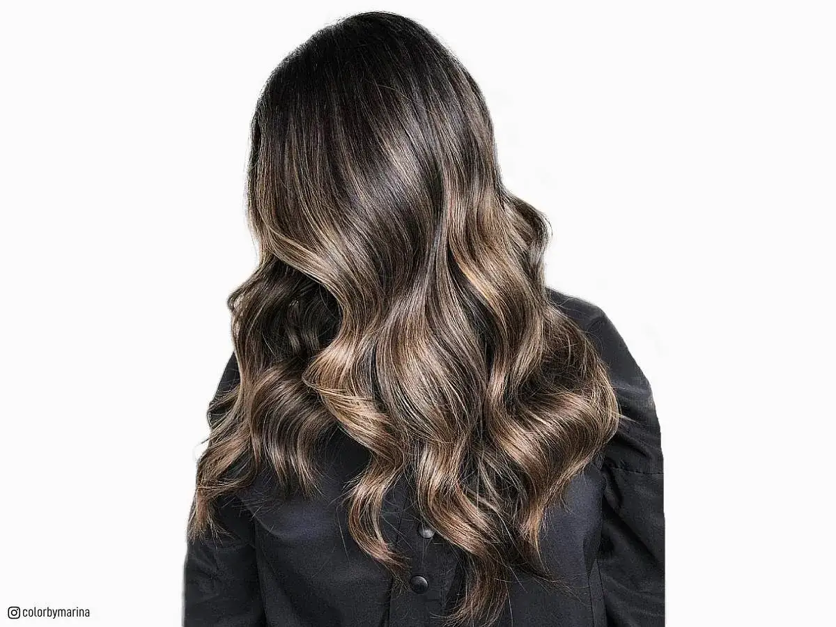 Pelo negro con mechas rubias, ondulado y brillante, cayendo sobre un vestido negro.
